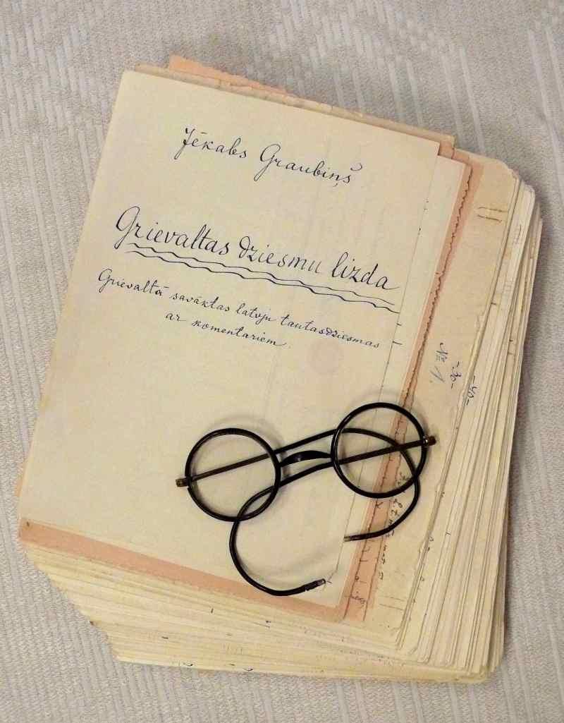 Grievaltas dziesmu lizdas manuskripts un Jēkaba Graubiņa apaļās brilles, kas